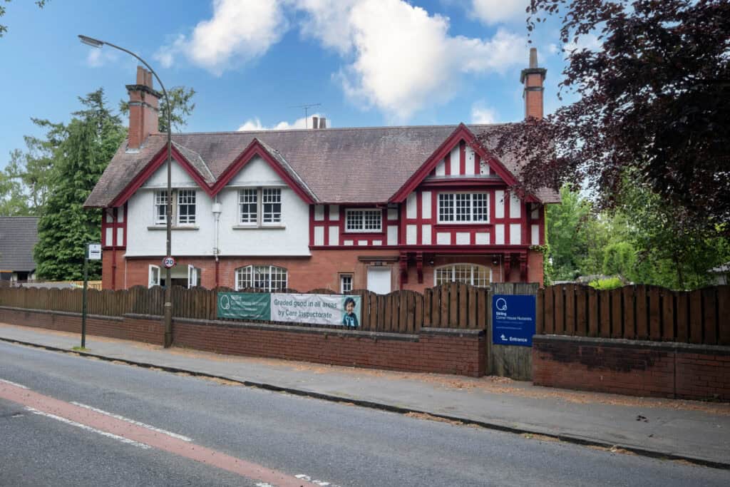 Bright red and white Tudor-style nursery building with welcoming entrance, surrounded by green trees, offering high-quality early childhood education and childcare services by Thrive Childcare.