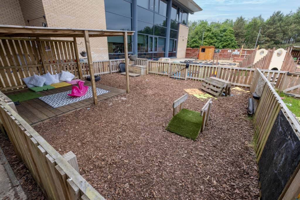 Bright outdoor childcare play area with wooden fencing, sensory play features, and shaded area, ideal for young children to explore and develop motor skills at Thrive Childcare.