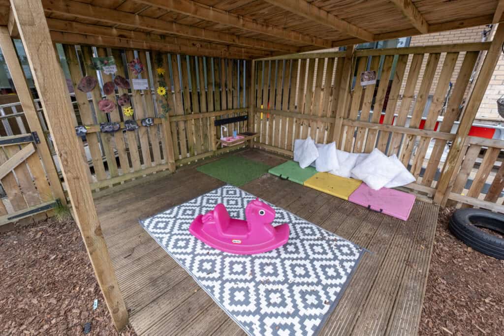 Bright outdoor children's play area with a pink rocking horse, soft mats, and climbing rocks, designed for early childhood development and outdoor fun at Thrive Childcare.