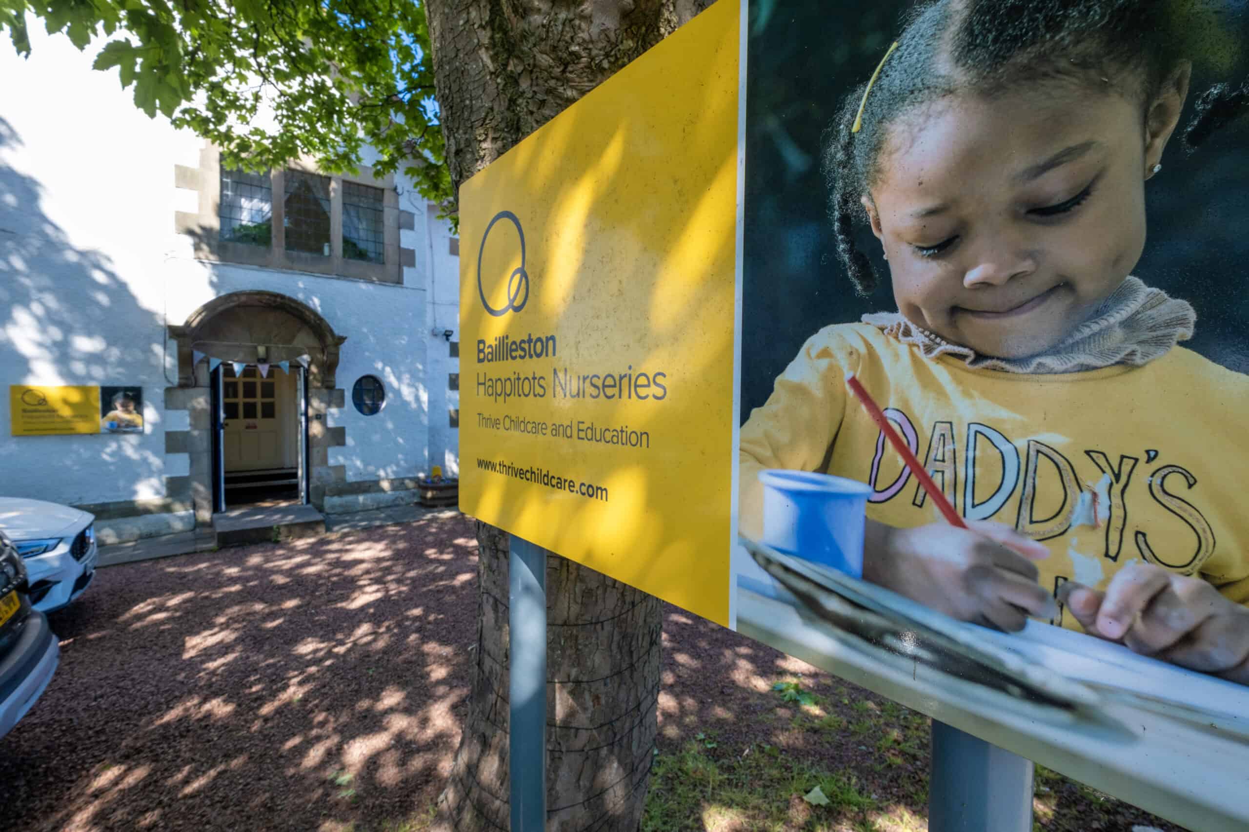 Bright yellow signage displaying "Bailleston Haptots Nurseries" outside Thrive Childcare and Education, highlighting dedicated childcare services in a welcoming environment.