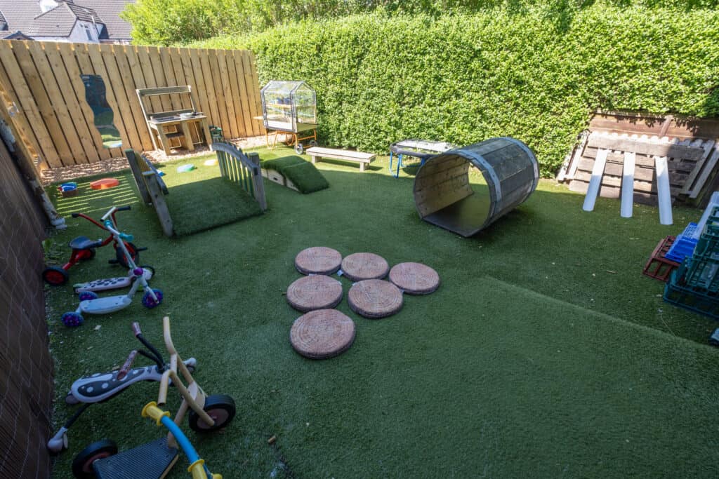 Bright outdoor play area at Thrive Childcare with artificial grass, climbing structures, tricycles, and sensory play equipment for children's active and imaginative outdoor activities.