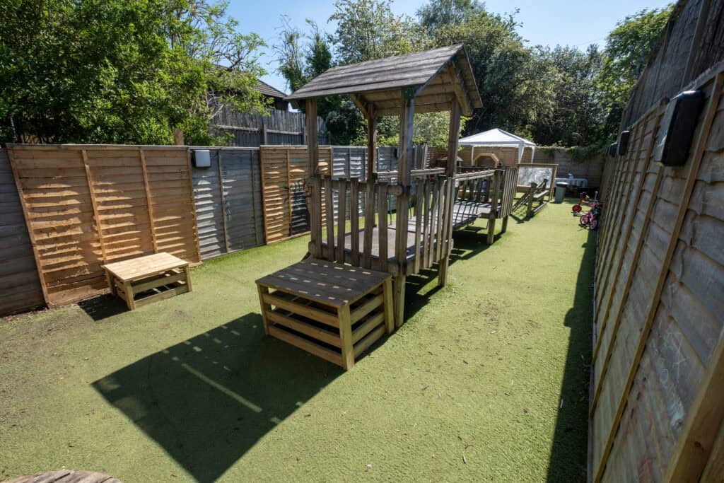 A colourful outdoor play area for kids with a wooden play structure, slides, and toys at Thrive Childcare. Ideal for children to enjoy supervised play and outdoor activities in a safe environment.