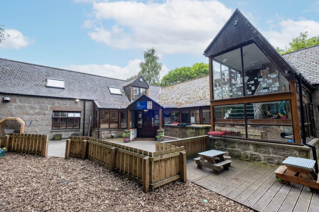 Bright outdoor playground area of Thrive Childcare with residential-style building, large glass windows, and wooden fencing, providing a safe and engaging environment for children's early education and development.