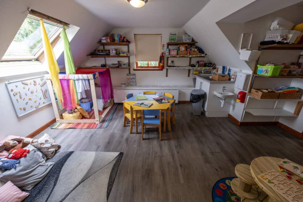 Bright indoor childcare room with colourful toys, play area, small table and chairs, storage shelves, and natural light from skylight windows, ideal for early childhood education and care.