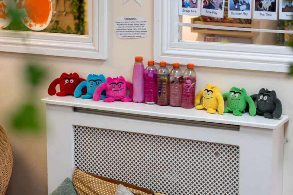 Brightly coloured plush toys and water bottles on a white radiator shelf at Thrive Childcare, creating a welcoming and playful environment for young children.
