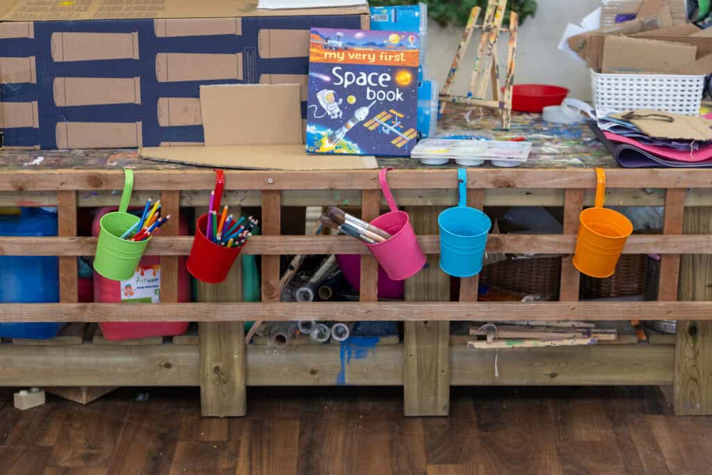 Colourful art supplies hanging from a wooden craft station at Thrive Childcare.