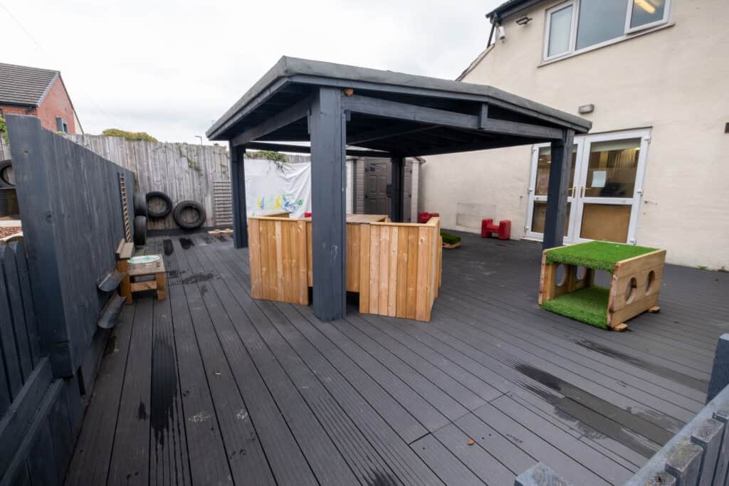 Bright outdoor childcare play area with wooden structures, rubber flooring, and climbing equipment, perfect for early childhood development at Thrive Childcare.
