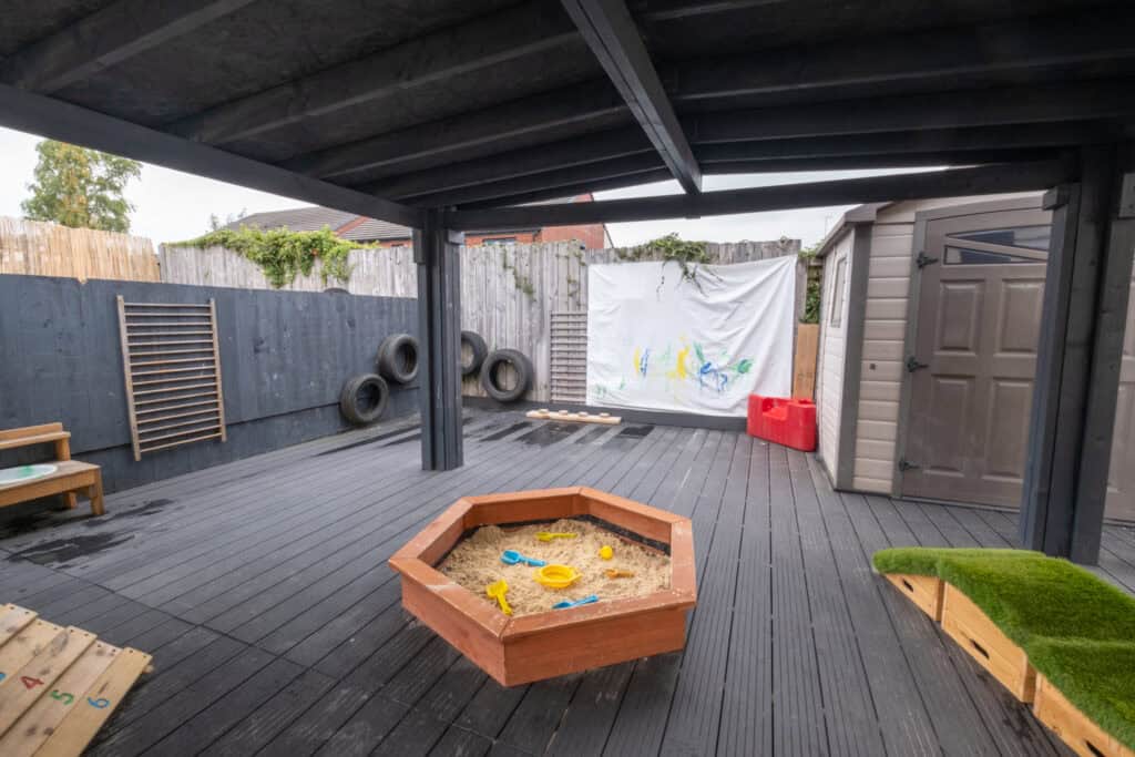Bright outdoor play area at Thrive Childcare, featuring sandpit, playhouse, climbing equipment, and toys, designed for children's outdoor activities and early childhood development.