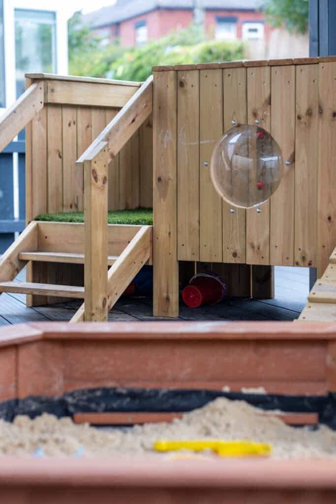 Bright wooden outdoor play structure with a slide, sandbox, and safe climbing areas at Thrive Childcare, fostering fun and development for young children.