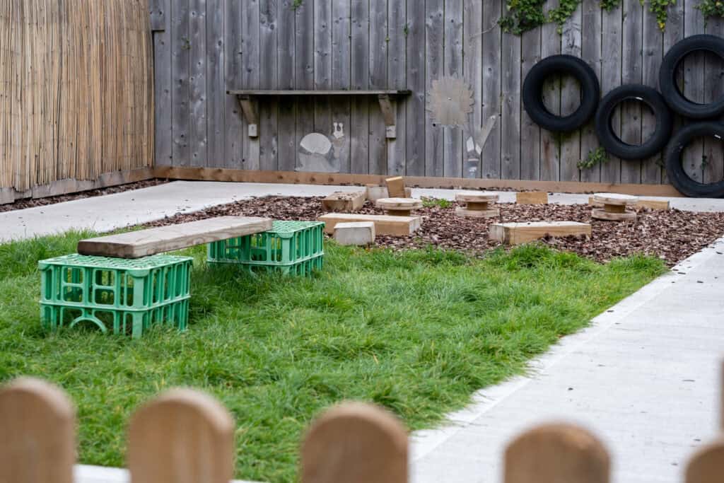 A colourful outdoor play area for children with grass, wooden activities, and tyre wall, providing a safe and engaging environment for early childhood play at Thrive Childcare.