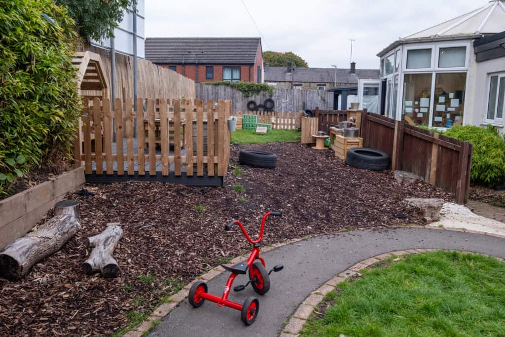 Bright outdoor childcare play area with wooden fencing, mini bikes, tires, and sensory play zones at Thrive Childcare in the UK. Suitable for young children to explore and enjoy outdoor activities.