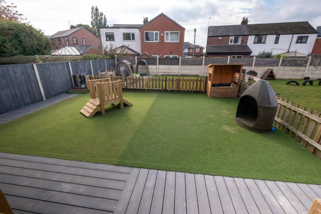 Bright, secure outdoor play area at Thrive Childcare featuring artificial grass, wooden play equipment, and sensory toys, providing a safe and engaging environment for children's outdoor activities.