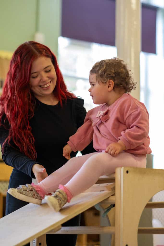 1. Friendly childcare provider assisting a toddler on an indoor play structure at Thrive Childcare in UK.