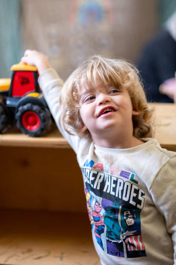 Bright-eyed young child playing with a toy tractor at Thrive Childcare, Exmouth. Engaging activities promote early childhood development and joyful learning in a safe, nurturing environment.