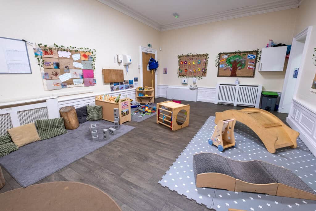 Bright and welcoming indoor childcare playroom with wooden toys, soft mats, and colourful artwork, designed to support early childhood development at Thrive Childcare.