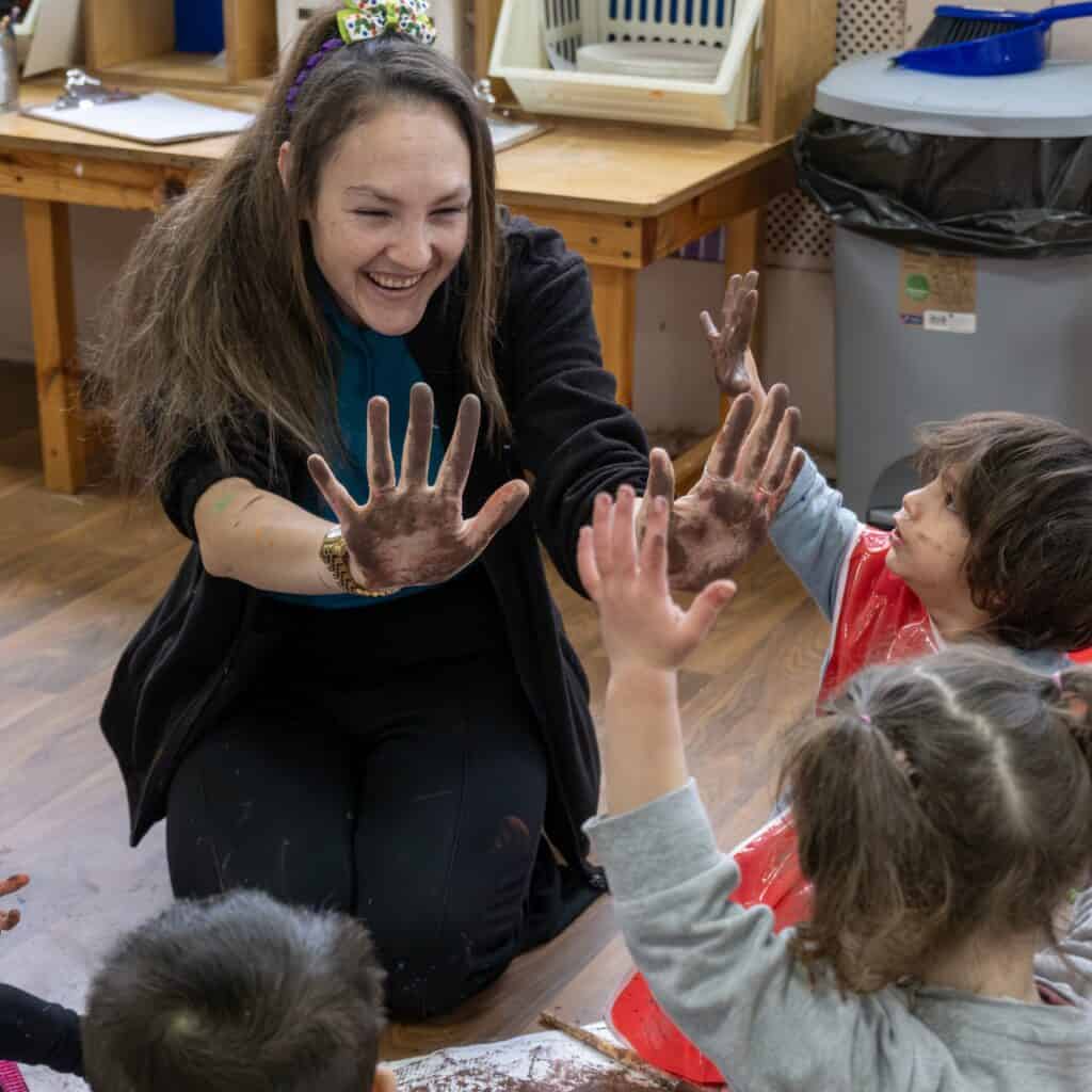 Bright and cheerful childcare environment featuring happy children engaging with a friendly caregiver during creative play activities at Thrive Childcare.