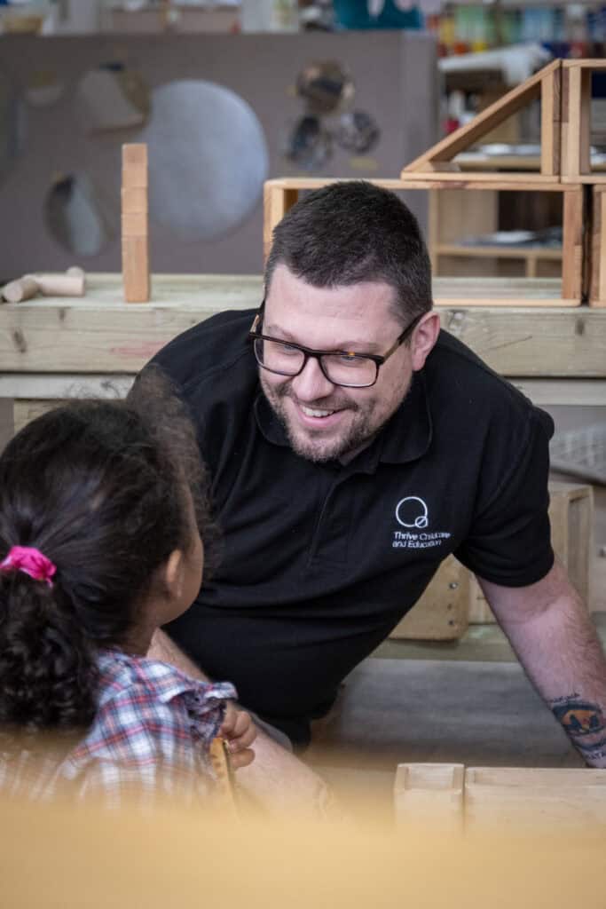A caring childcare professional engaging with a young girl in a colourful classroom setting at Thrive Childcare, promoting early childhood education and development.