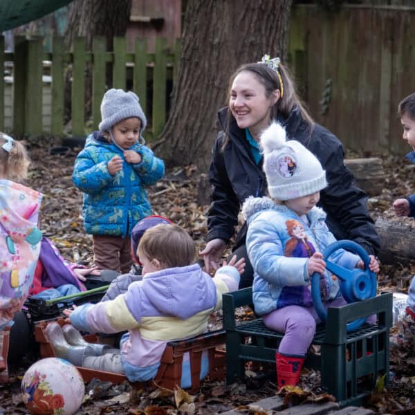 Children playing outdoors with caregiver at Thrive Childcare, engaging in imaginative and outdoor activities in a natural play area.