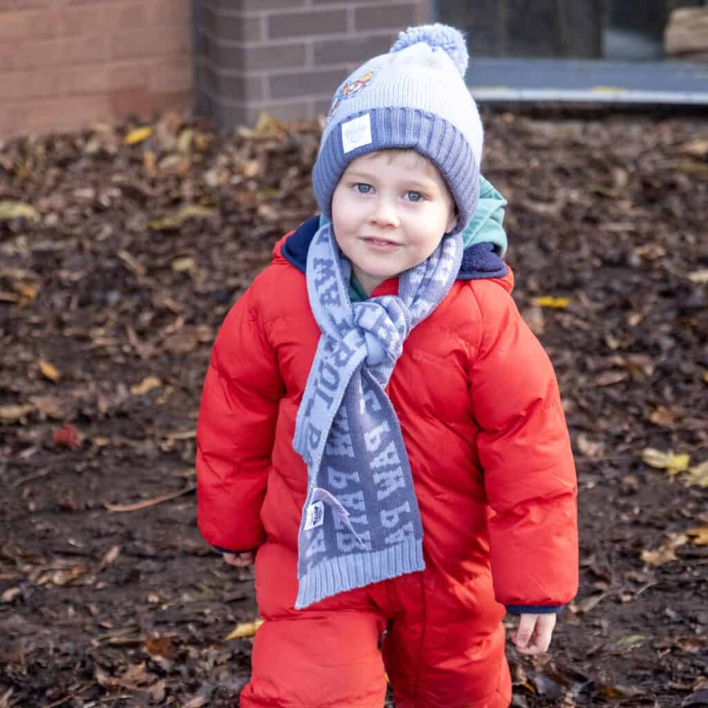 Young child in warm winter clothing playing outdoors at Thrive Childcare, enjoying outdoor activities and exploration.