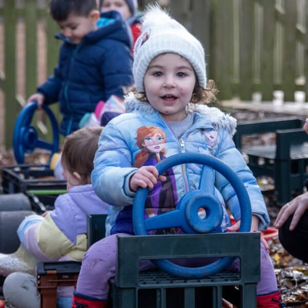 Bright young children playing outdoors in a woodland area, enjoying supervised activities at Thrive Childcare. Engaging in imaginative play with toys and fresh air, supporting early childhood development and social skills.
