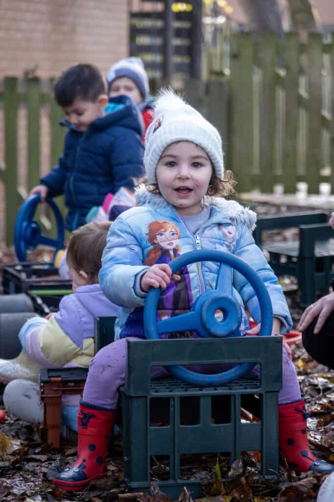 Bright young children playing outdoors in a woodland area, enjoying supervised activities at Thrive Childcare. Engaging in imaginative play with toys and fresh air, supporting early childhood development and social skills.