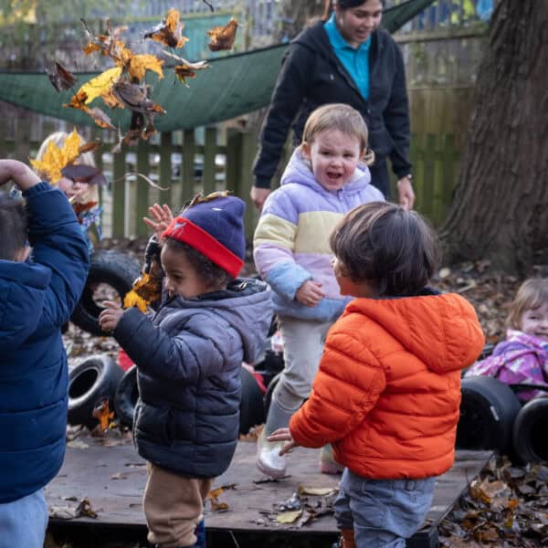 Playing outdoors with children in autumn leaves at Thrive Childcare, promoting child development through nature-based activities.