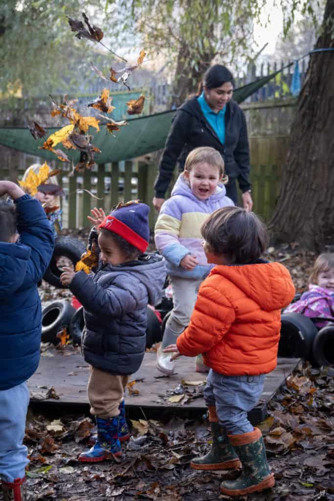 Playing outdoors with children in autumn leaves at Thrive Childcare, promoting child development through nature-based activities.
