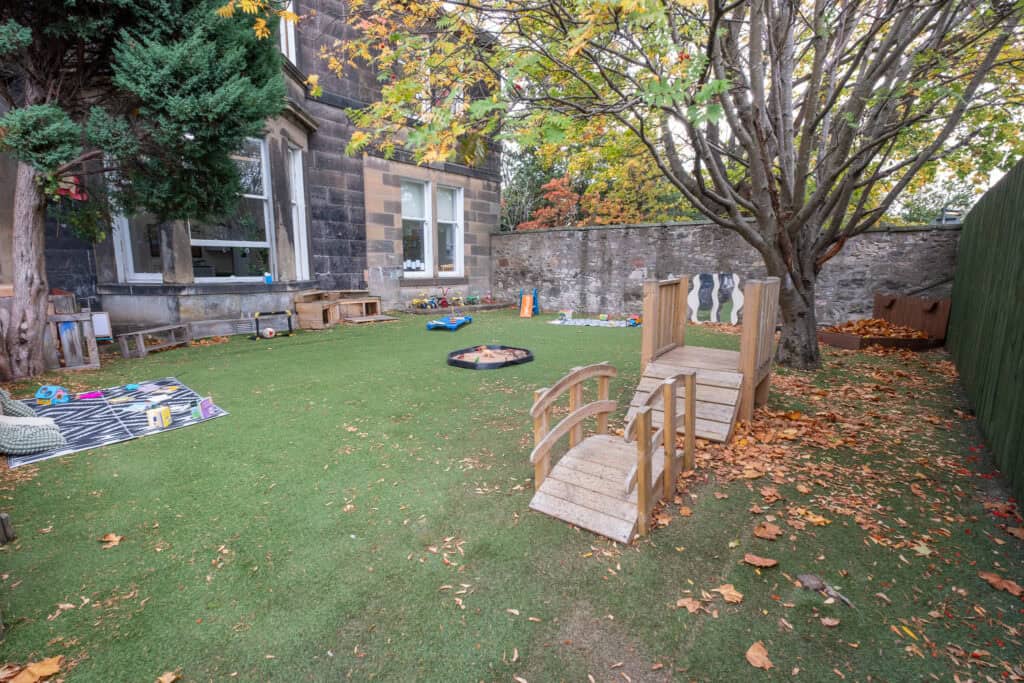 Bright outdoor childcare play area with artificial grass, children's toys, and sandbox, offering a safe and engaging environment for learning and outdoor activities at Thrive Childcare.