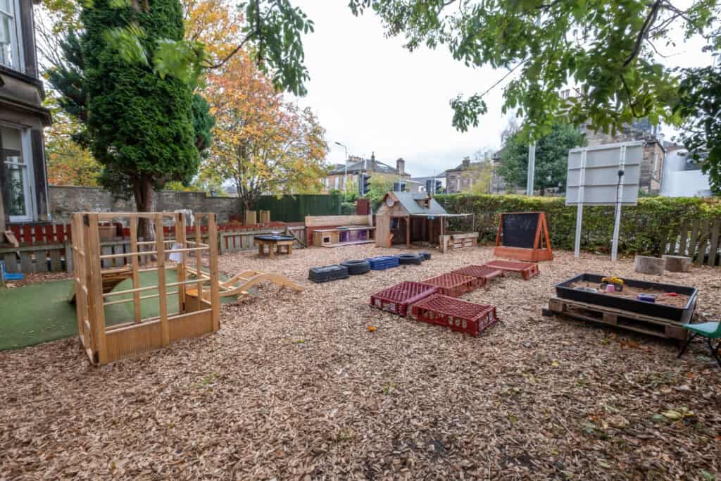 Colourful outdoor play area at Thrive Childcare in Scotland with wooden play structures, sandpit, and tires, designed for early childhood development and outdoor activities.