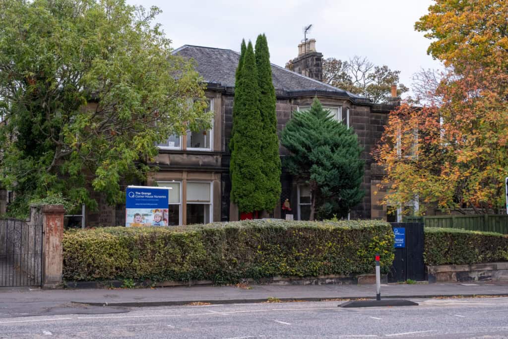Bright, welcoming nursery building surrounded by lush trees and greenery, featuring a colourful sign for Thrive Childcare, providing high-quality early childhood education and nursery care in a friendly environment.