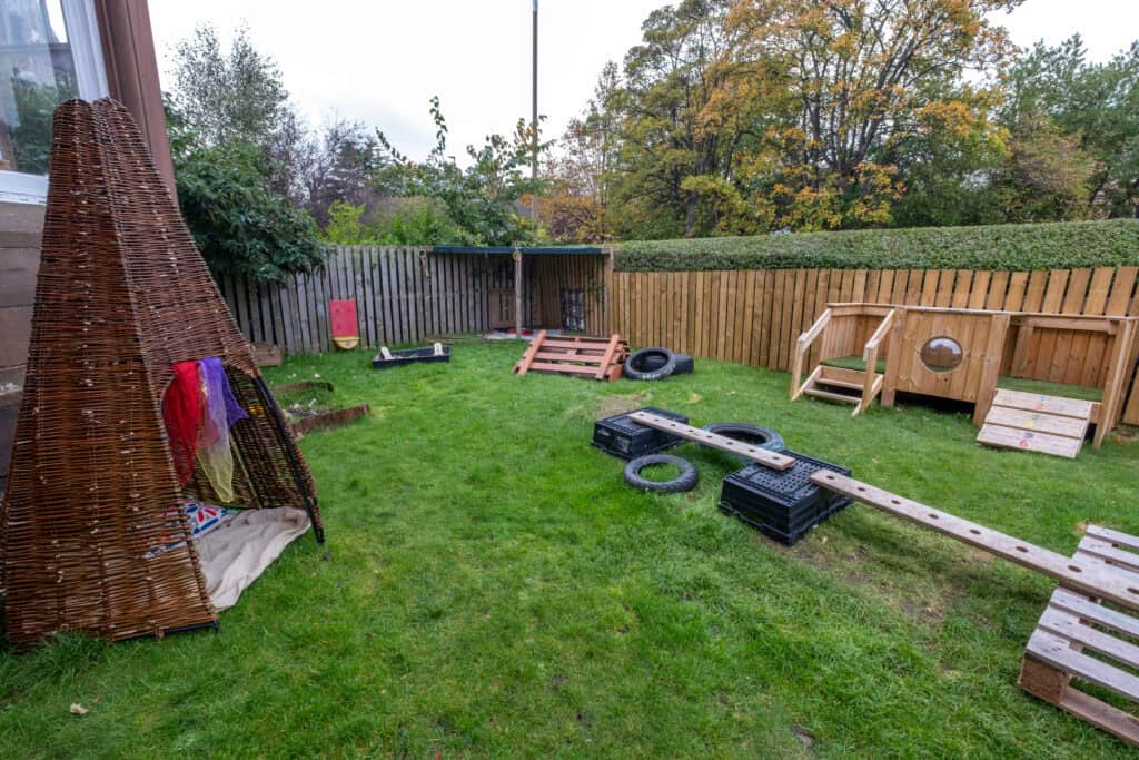 Colourful outdoor play area with wooden structures, tyres, and playground equipment at Thrive Childcare, offering a safe environment for children to explore and develop through fun, outdoor activities.
