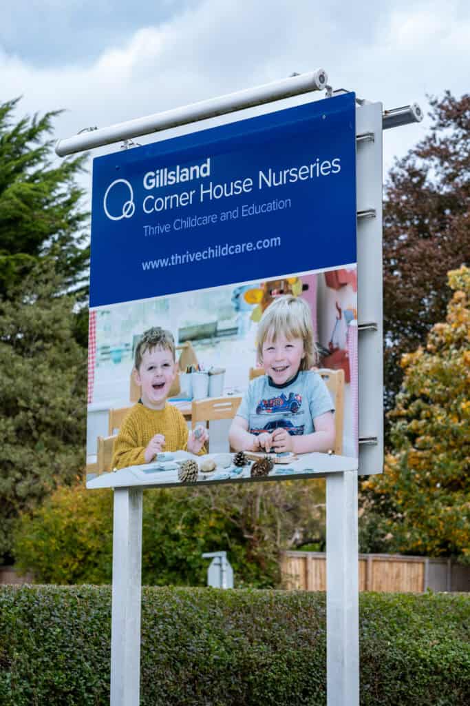 Bright outdoor sign for Thrive Childcare, Gillsland Corner House Nurseries, promoting early childhood education and nursery services in a green leafy setting.
