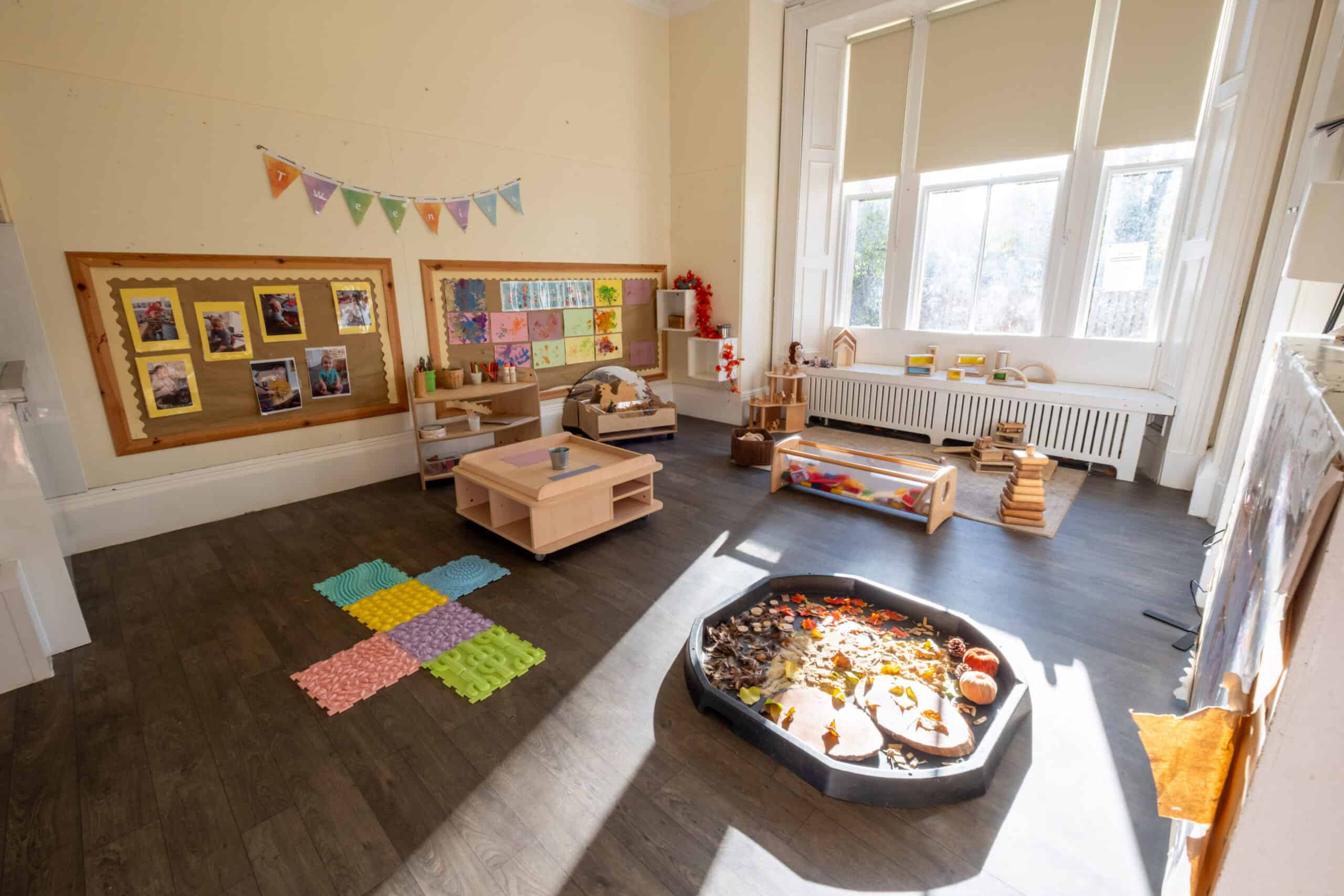 Bright indoor childcare playroom with toys, art displays, and natural sunlight, ideal for early childhood development and early learning at Thrive Childcare, fostering a safe, nurturing environment.