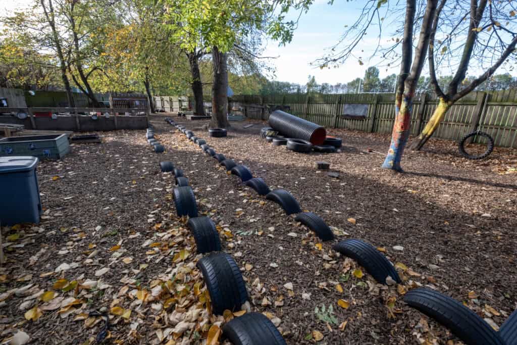 Climbing adventure for children at Thrive Childcare outdoor play area with tire obstacle course and natural surroundings for outdoor learning and physical development.