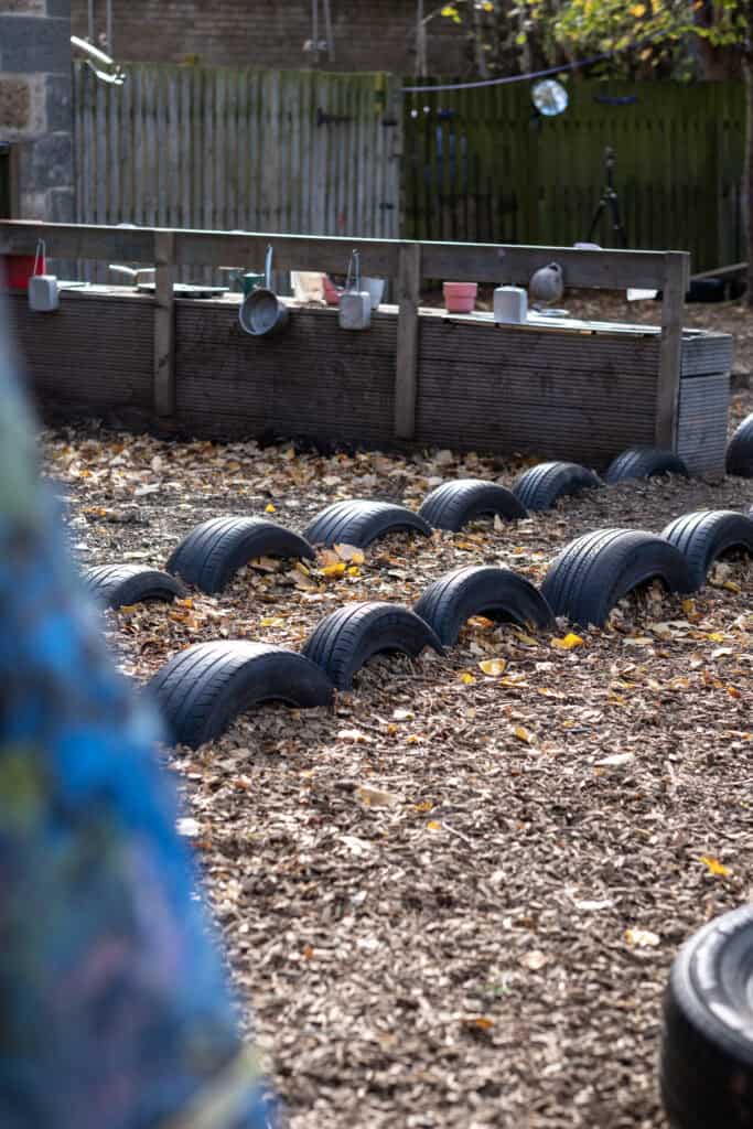 A safe outdoor play area at Thrive Childcare with a tire obstacle course and raised garden beds, perfect for children's physical activity and creative play in a nurturing environment.