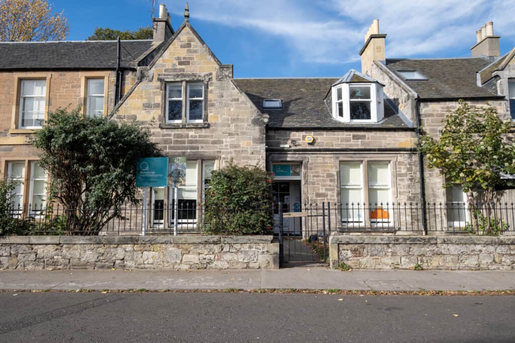 Bright stone-built childcare centre with large windows and a welcoming entrance, offering a safe, nurturing environment for early childhood education in a charming community setting.