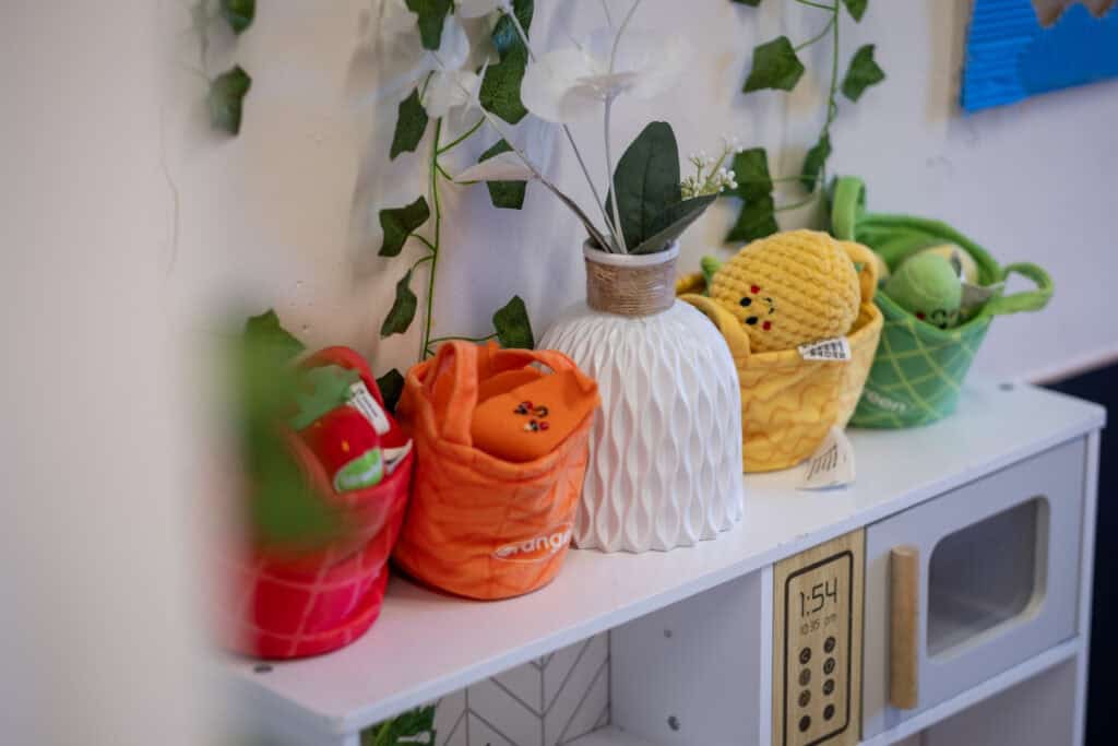 Brightly coloured plush toys and baskets on a white play kitchen in a childcare centre, promoting a fun and nurturing environment for young children.