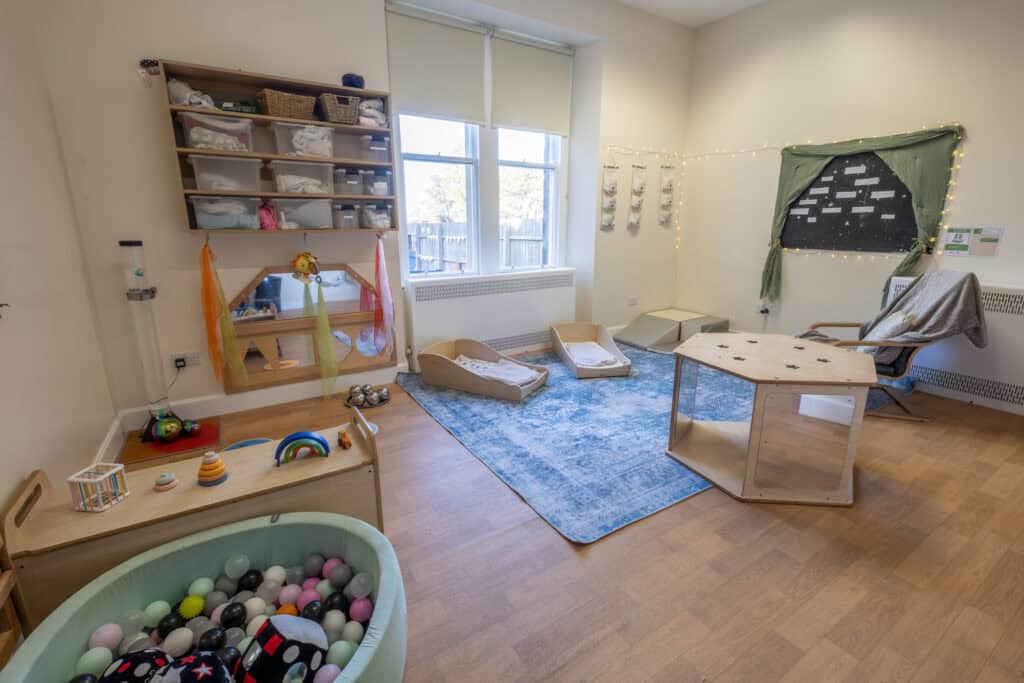Bright childcare indoor playroom with soft toys, baby cribs, and activity areas, designed for early childhood development and nurturing children’s growth at Thrive Childcare.