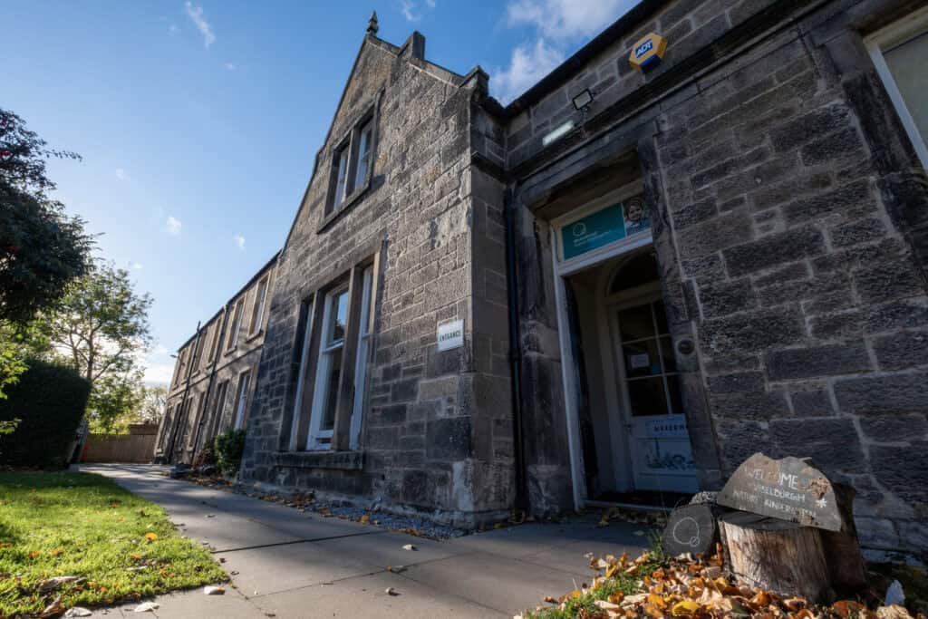 Bright stone building of Thrive Childcare nursery with welcoming entrance, large windows, and autumn leaves outside, providing high-quality early years education and nurturing environment for children in Edinburgh.