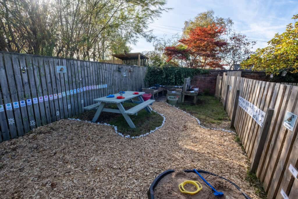 1. Bright outdoor childcare play area with sandpit, wooden fencing, and toddler activities for early childhood development and outdoor learning in a safe environment.