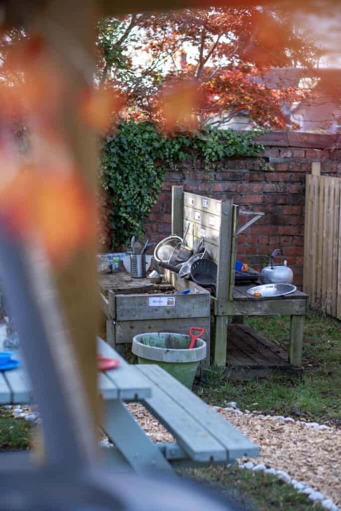 1. Outdoor children’s play kitchen with toy dishes, utensils, and a wooden sink in a colourful garden setting at Thrive Childcare.