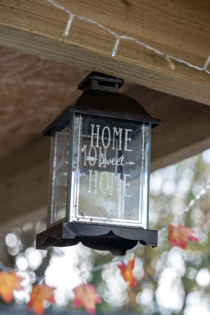 1. Cute outdoor lantern with "Home Sweet Home" message, hanging under a wooden shelter, decorated with string lights, in a welcoming childcare or family setting.