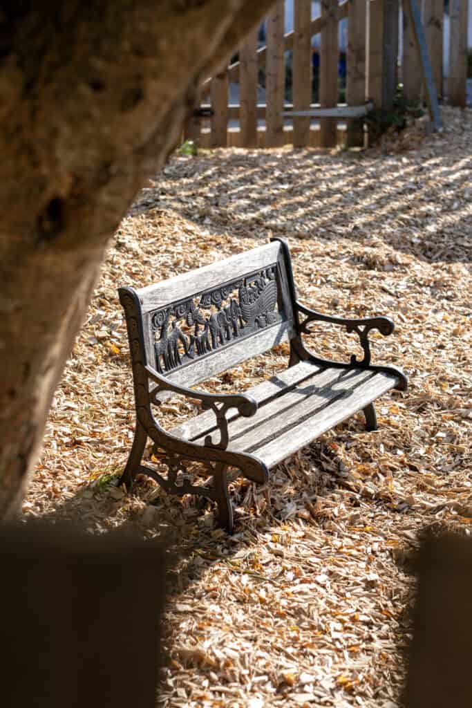 A decorative outdoor bench in a playground surrounded by fallen leaves, providing a relaxing space for children at Thrive Childcare. Perfect for outdoor activities and enjoying nature.