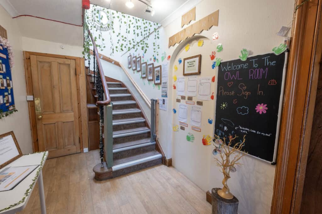 Bright nursery entrance with colourful handprints, welcoming blackboard sign, and staircase at Thrive Childcare, highlighting a safe and engaging environment for early childhood education and care.