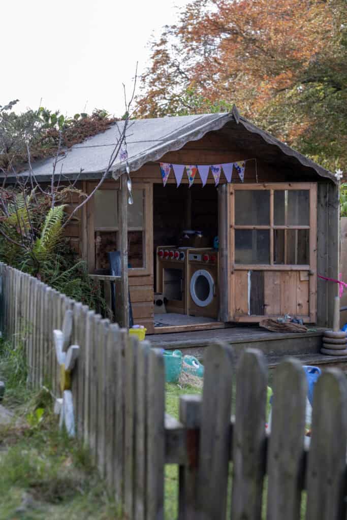 Colourful children's outdoor playhouse with miniature kitchen, surrounded by a garden, perfect for early childhood development, outdoor play, and child-friendly learning environments.