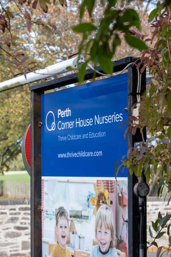 Outdoor nursery sign featuring the Thrive Childcare logo and children’s photo, highlighting Perth Corner House Nurseries' focus on early years education and care in a welcoming environment.