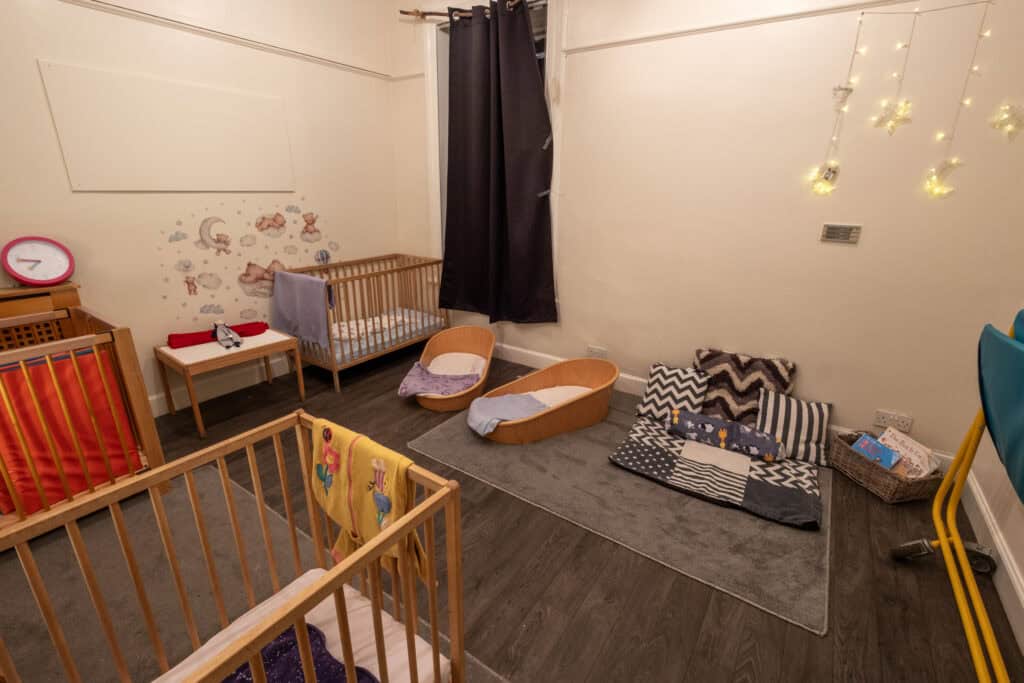 Soft playroom at Thrive Childcare featuring cribs, cozy bedding, toys, and nursery decor for infants and toddlers, creating a safe and nurturing environment for young children.