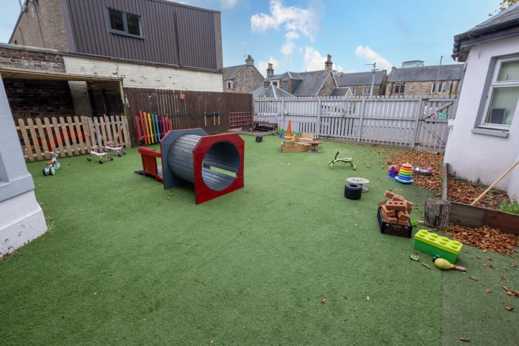 Bright outdoor childcare play area with artificial grass, colourful toys, and safe fencing, ideal for early childhood development and fun at Thrive Childcare.
