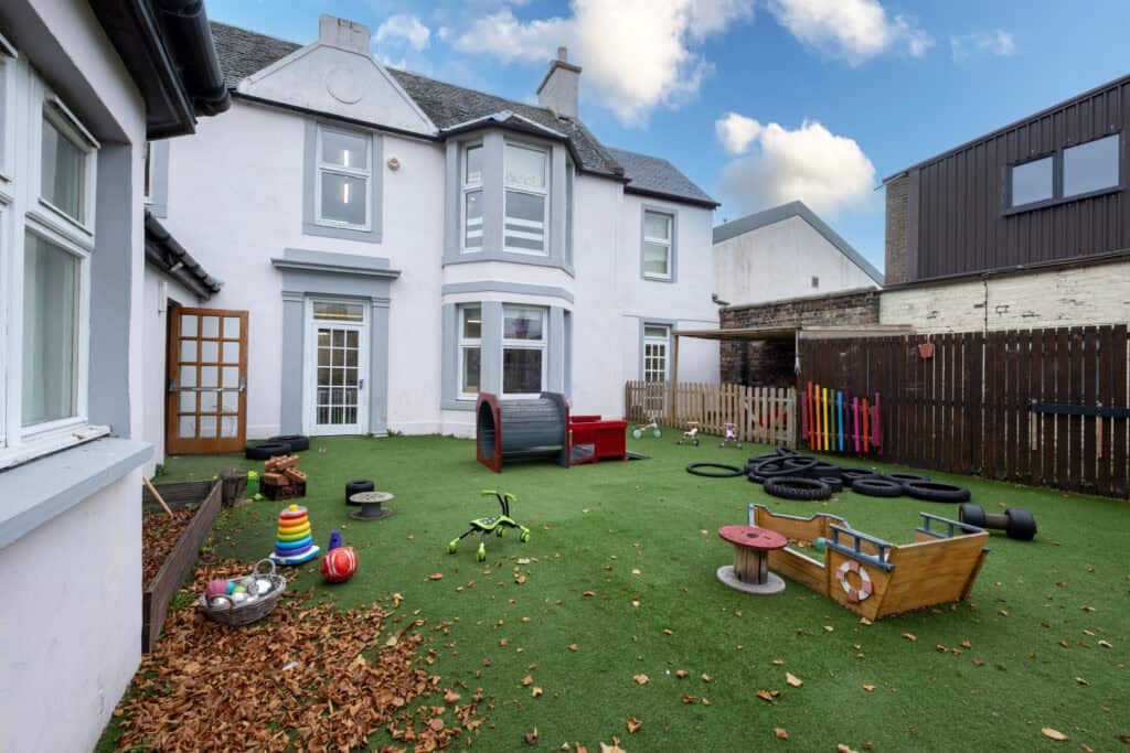 Bright outdoor childcare play area with artificial turf, toys, and play equipment at Thrive Childcare centre in a residential setting, ideal for early childhood development and nursery activities.