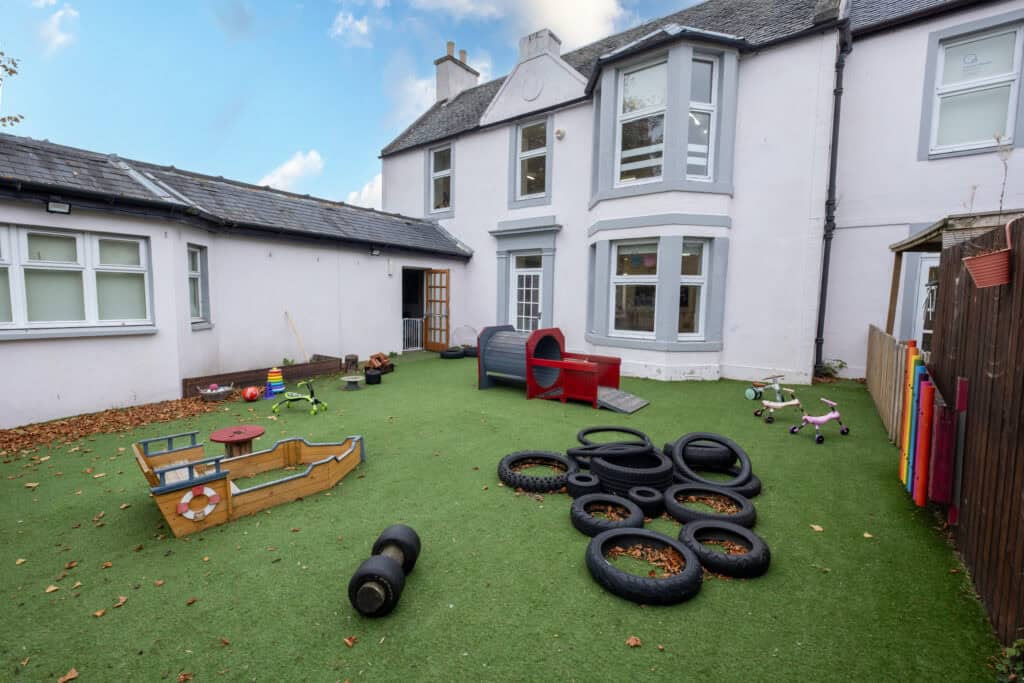 Colourful outdoor childcare play area with toys, tyres, mini bikes, and a playhouse for children at Thrive Childcare, offering a safe and engaging environment for early childhood development.